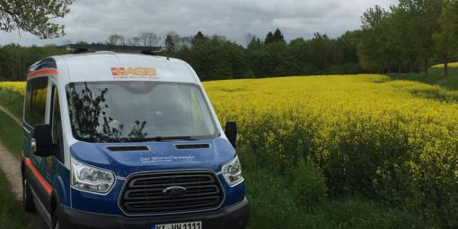 Symbolbild 1: Der ASB-Wünschewagen am blühenden Rapsfeld.